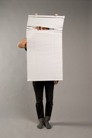 man with venetian blinds hanging in front of his body, peaking through them