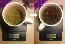 Photograph of coffee mug with green beans on left, roasted on right, Scale beneath mug indicates 100g of green, 85 of roasted
