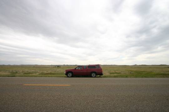 red truck parked on side of highway with fields in background